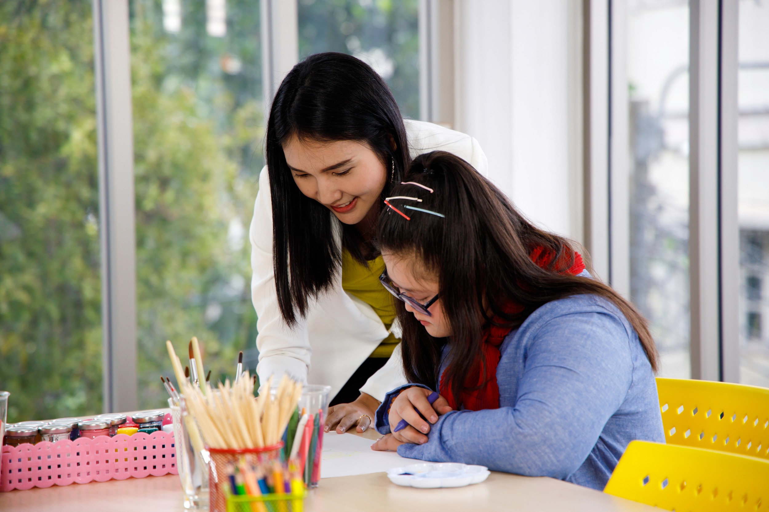 Teacher teaches art to girl with Down's syndrome in classroom. Concept disabled kid learning.