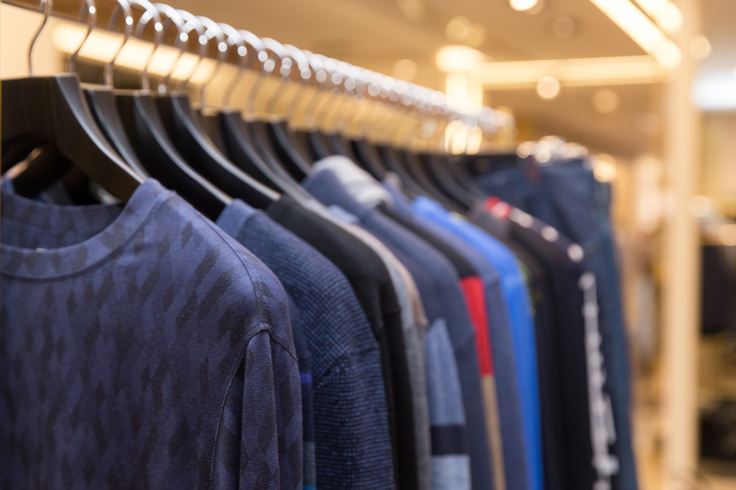 Men sweaters and shirts in different colors on hangers in a retail clothes store. Beautiful clothes for winter autumn season. Fashion industry for men.